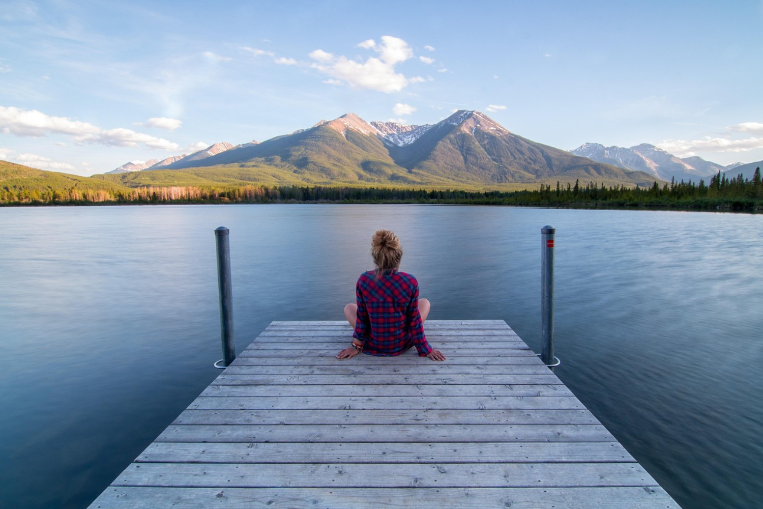 Woman sits quietly on dock facing mountain view
