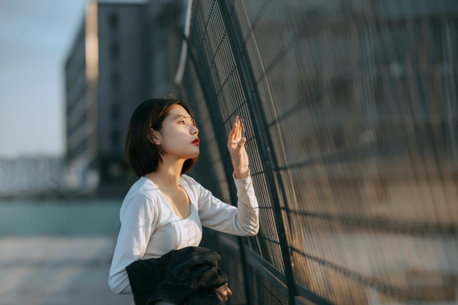 Woman gazes through fence under golden sunlight