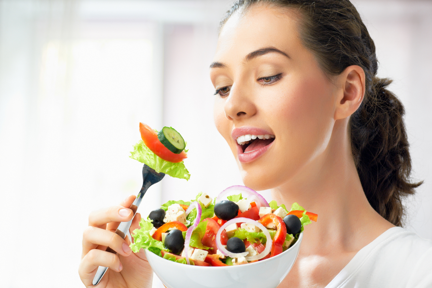 Smiling woman eating a colorful vegetable salad.