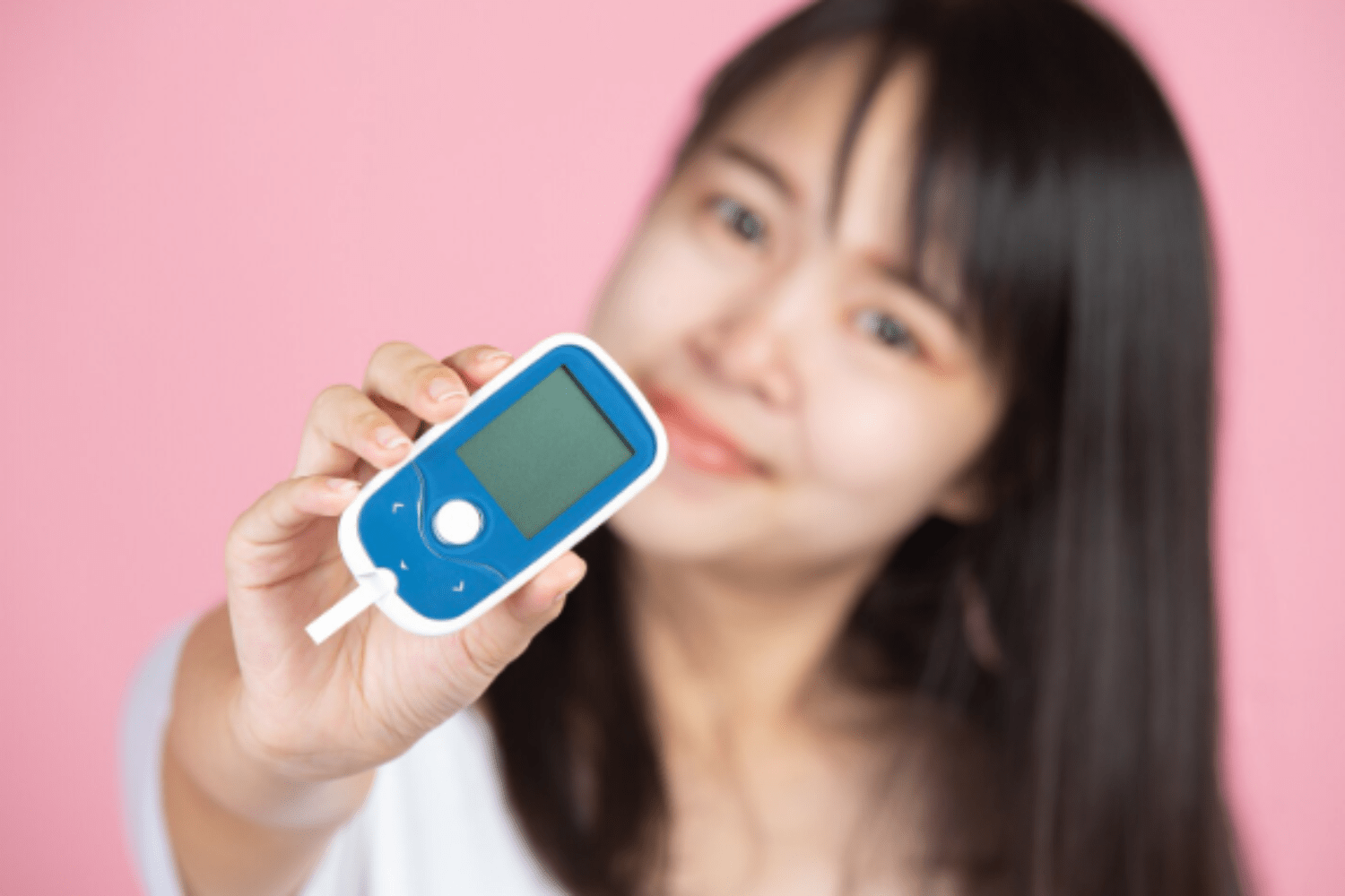 Woman holding glucose monitor with pink background
