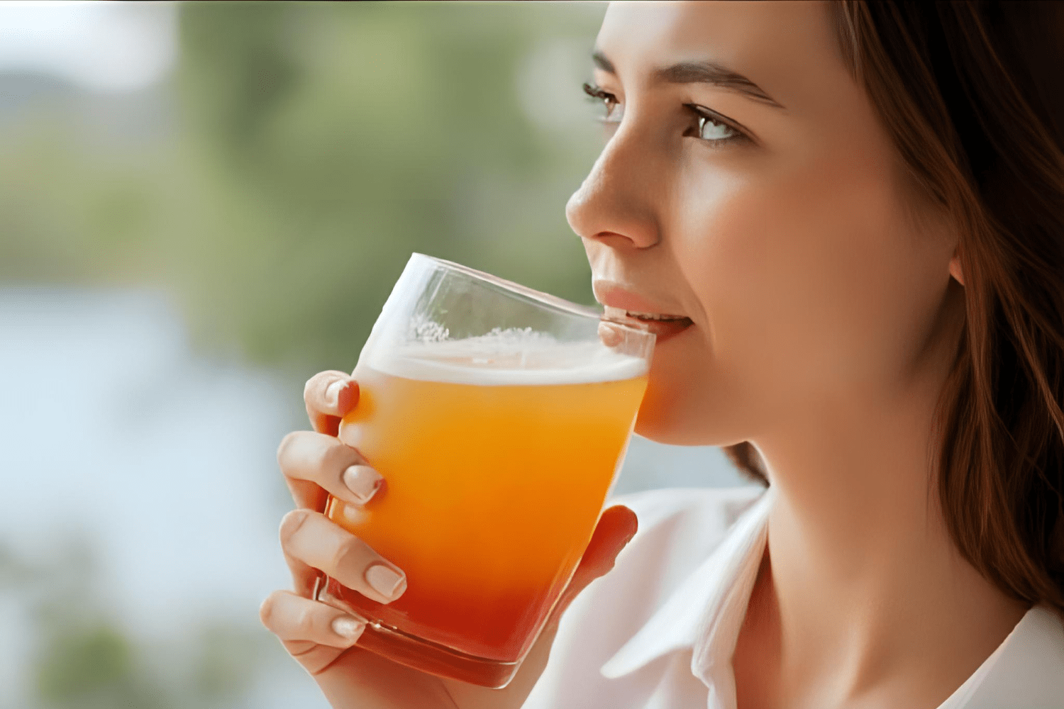 Woman sipping kombucha beside a window view
